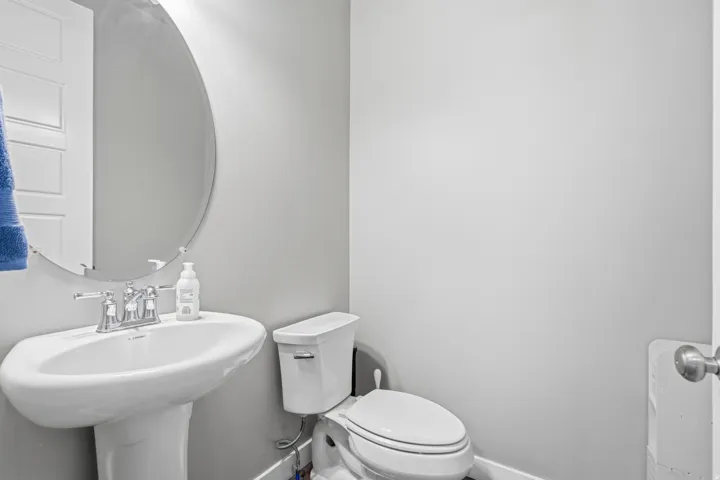Pedestal sink with chrome faucet, oval frameless mirror, and a white two-piece toilet