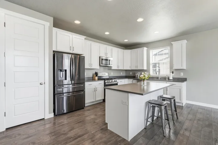 White shaker cabinetry, stainless steel appliances, central island with seating, wood-finish flooring, and recessed lighting