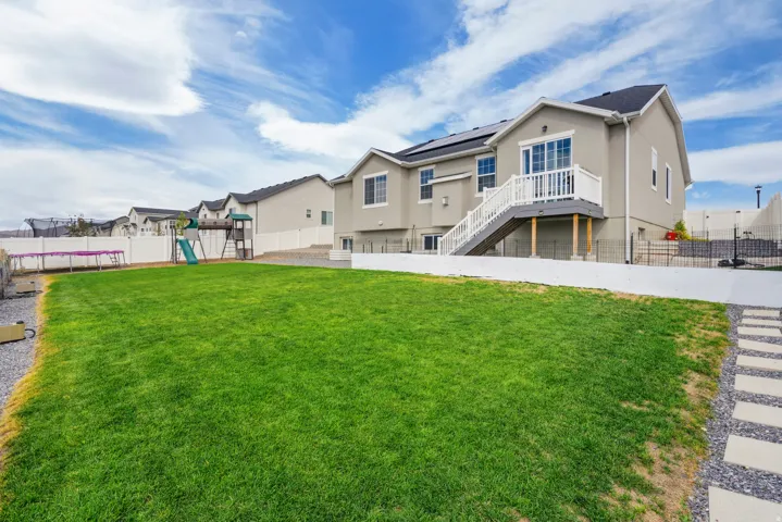 Expansive manicured lawn with mature landscaping, stone pathway, and composite deck with metal railings