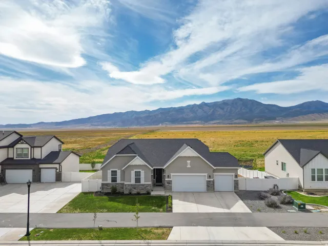 Contemporary ranch-style residence featuring a two-car garage, stone and stucco exterior, and a dark shingle roof