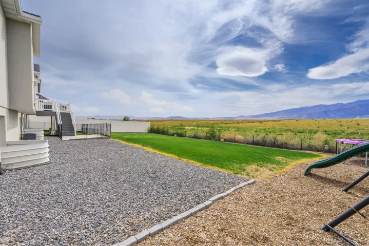Expansive backyard featuring a gravel and wood chip ground cover, a manicured lawn, and a white privacy fence
