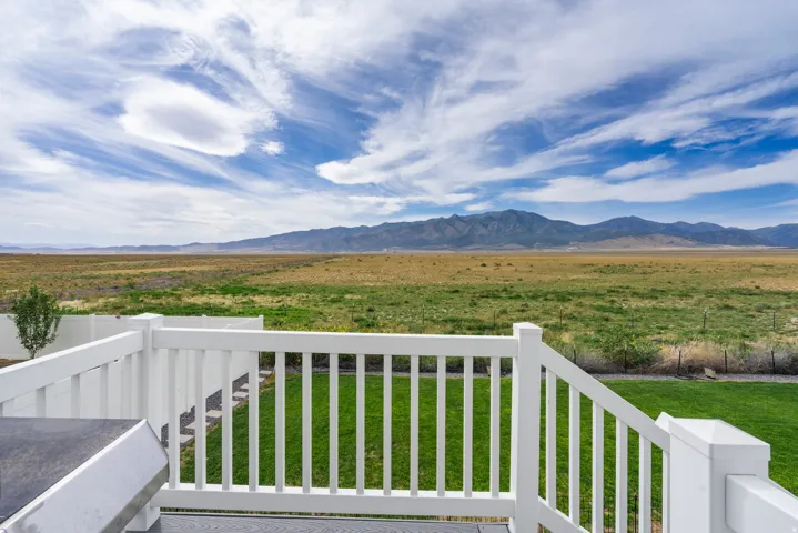 Expansive mountain range backdrop, vast natural landscape, groomed lawn, white privacy fencing, and a durable deck railing