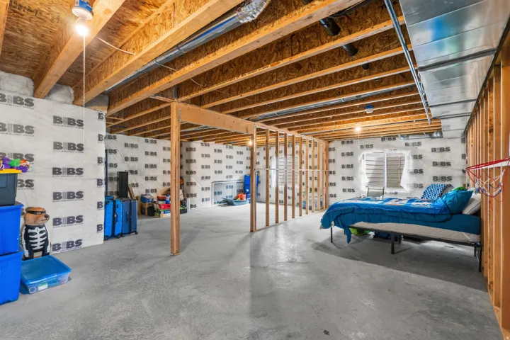 Unfinished basement featuring exposed wood joists, concrete flooring, stud walls, and insulated wall panels