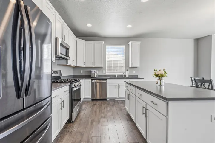 Kitchen with white cabinetry, stainless steel appliances, dark countertops, wood-finish flooring, and recessed lighting