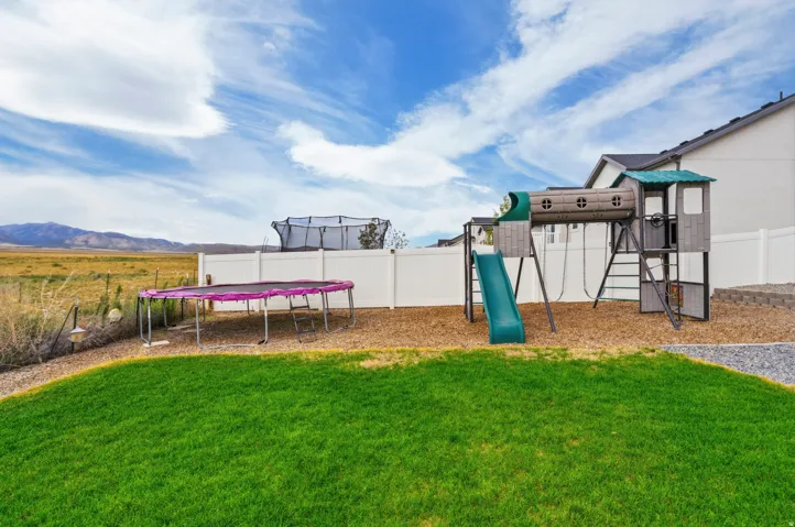 Expansive backyard featuring a manicured lawn, white privacy fencing, and a built-in playset with slide
