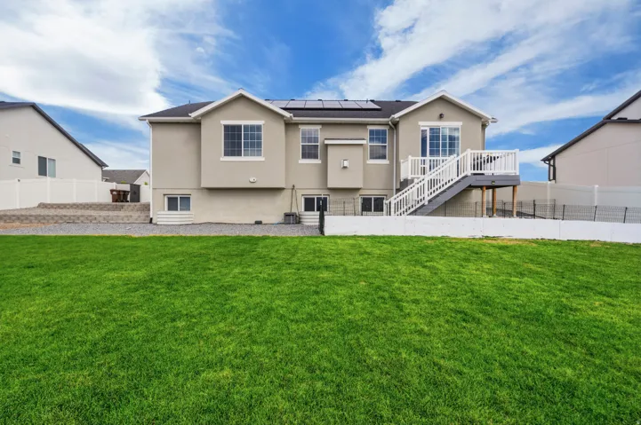 Expansive lawn with a stucco exterior, upper-level deck, white railing, and solar panels