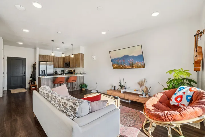 Open-concept living space with wood-finish flooring, recessed lighting, and a kitchen featuring wood cabinetry, stainless steel appliances, and a breakfast bar with pendant lighting