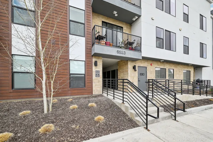 Modern building exterior with wood-finish siding, stone accents, multiple large windows, and a private balcony