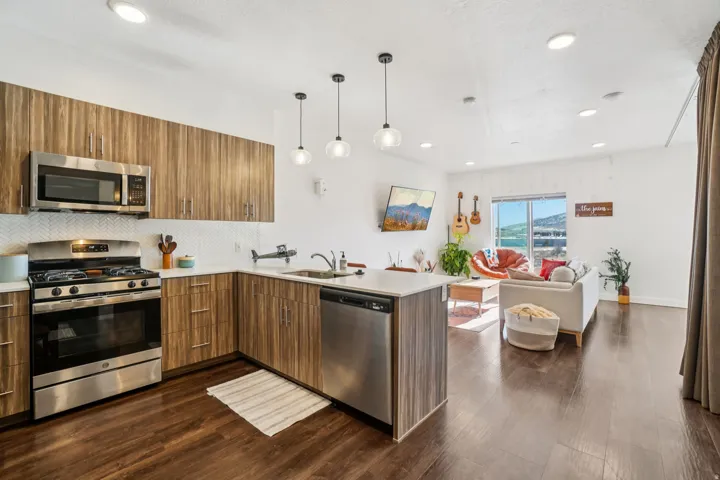 Open-concept living area with wood-finish flooring, recessed lighting, and a kitchen featuring stainless steel appliances, wood-grain cabinetry, and a subway tile backsplash