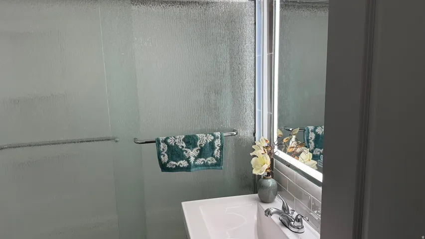 Frosted glass shower enclosure with chrome towel bar, single basin vanity with chrome faucet, and subway tile backsplash