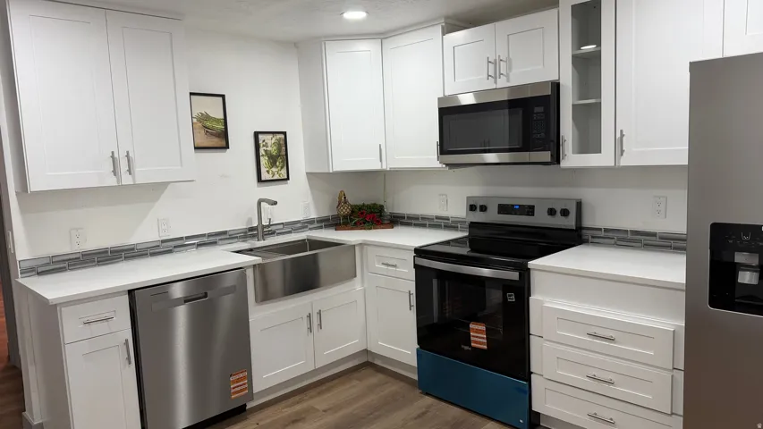 White cabinetry with stainless steel appliances, a farmhouse sink, and wood-finish flooring