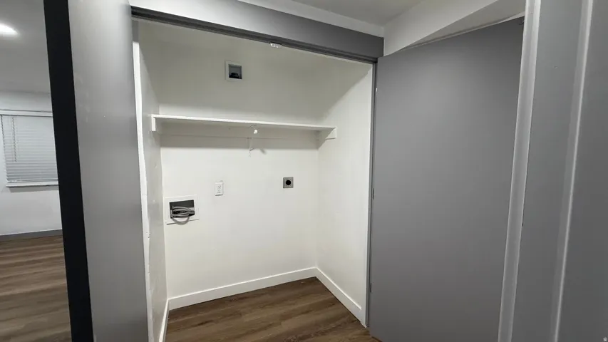 Laundry closet with hookups, built-in shelving, and wood-finish flooring