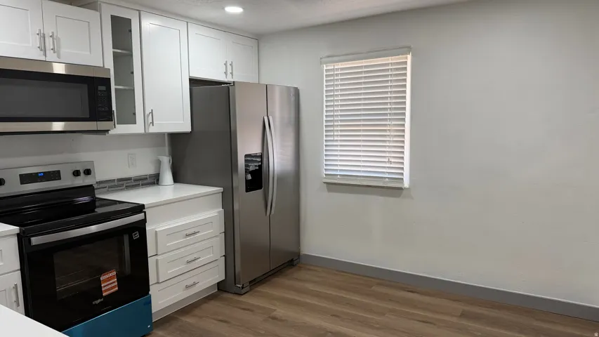 Kitchen featuring wood-finish flooring, white cabinetry, stainless steel appliances, and light countertops