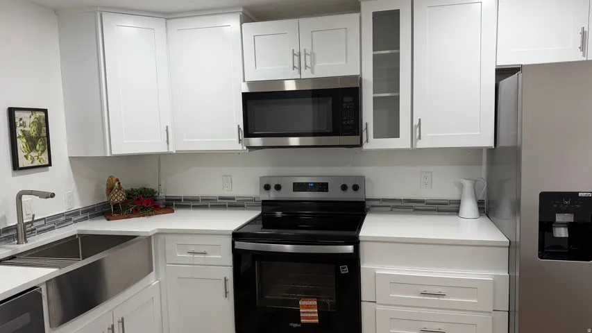White cabinetry with brushed nickel hardware, stainless steel apron-front sink, white countertops, tile backsplash, and stainless steel appliances