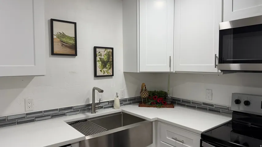 White shaker-style cabinetry, stainless steel sink, brushed nickel faucet, light-toned countertop, and a tiled backsplash