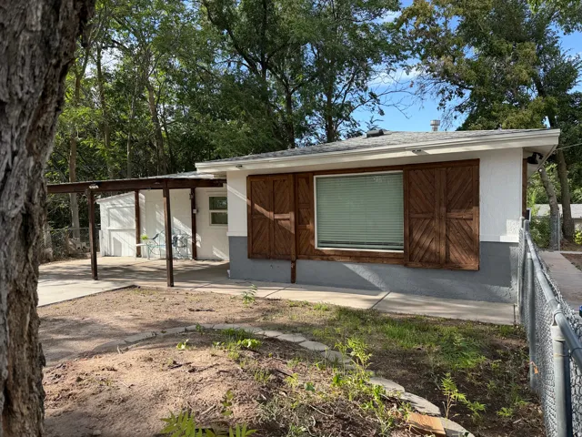 Modern single-story residence featuring a clean-lined exterior with board-and-batten wood doors, expansive front-facing window with operable shutters, and a covered carport structure