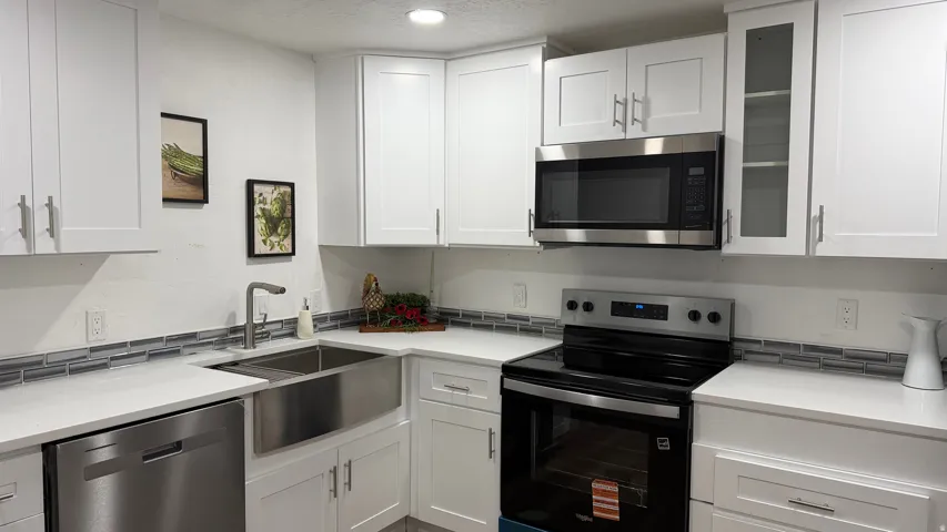 Modern kitchen featuring white cabinetry with stainless steel appliances, including a black electric range and matching microwave hood