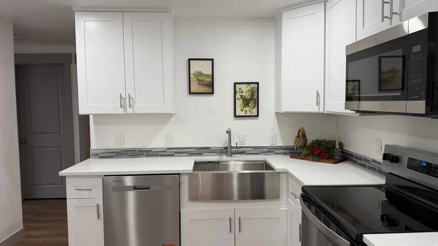 White shaker-style cabinetry, stainless steel appliances, quartz countertops, a tile backsplash, and a farmhouse-style sink