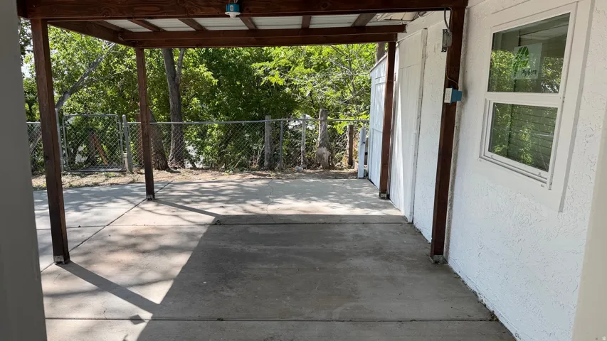 Covered patio area with concrete flooring, framed by a chain-link fence, and featuring an exterior window