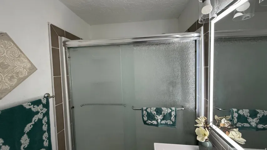Frosted glass shower enclosure with chrome framing, bordered by vertical wall tile