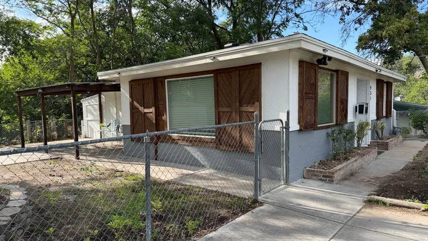 Exterior features include wood-finish shutters, a covered patio, a chain-link fence, and a concrete walkway