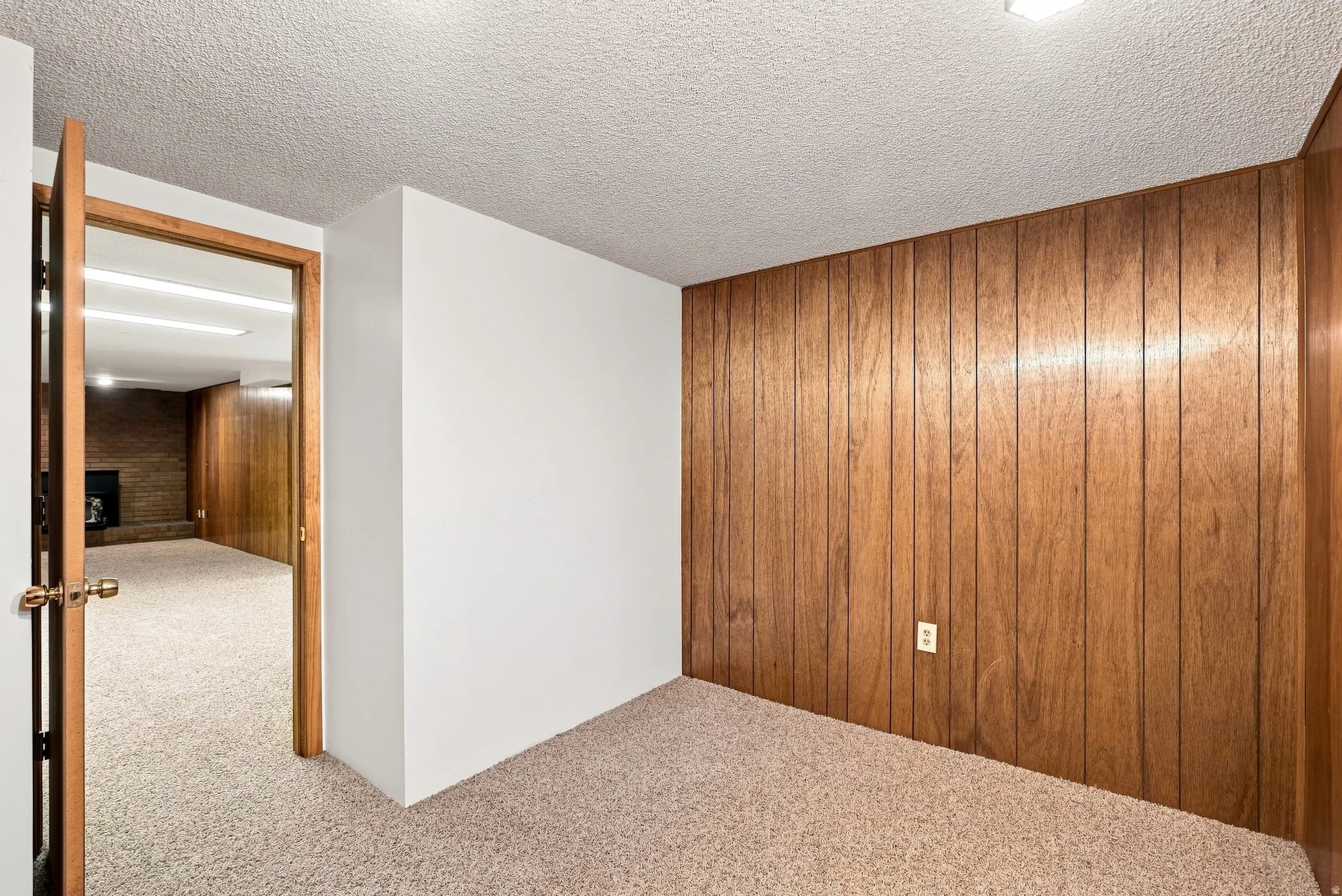 Wood-paneled accent wall, neutral carpeting, white painted walls, wood-finish doorframe