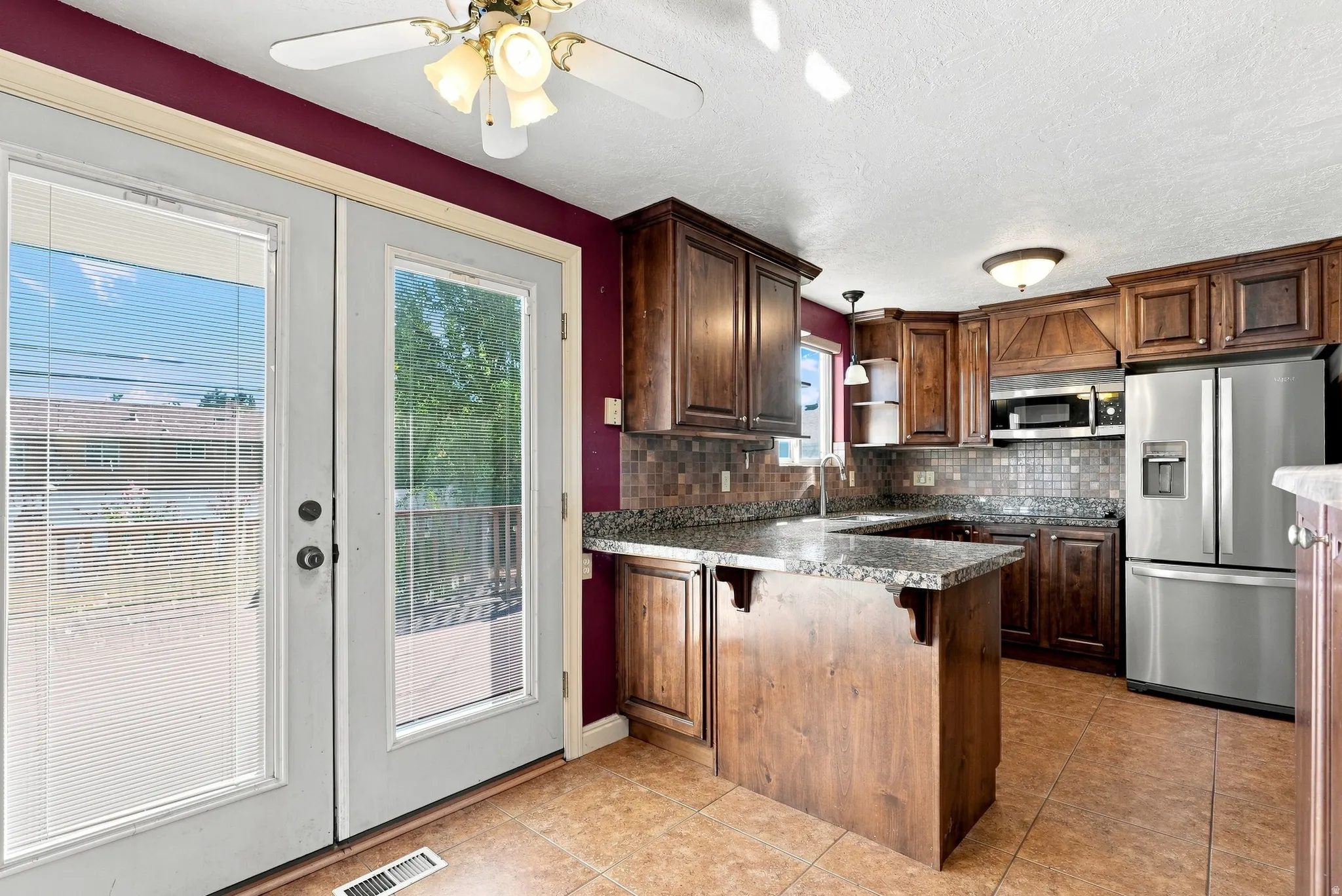 Kitchen featuring wood cabinetry, stainless steel appliances, a granite-finish countertop, a tile backsplash, and a center island