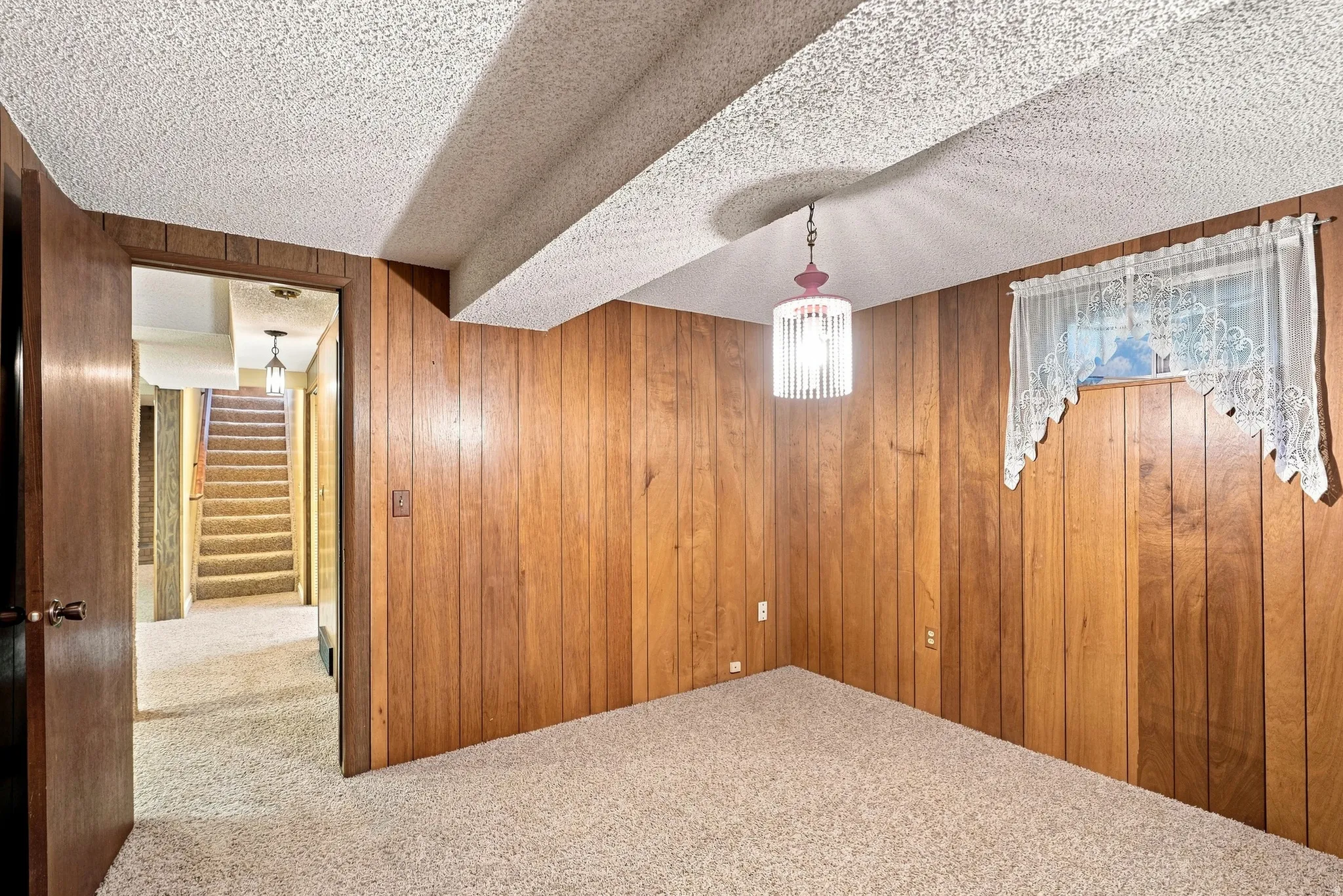 Carpeted flooring with wood-paneled walls, a textured ceiling, and a hanging light fixture