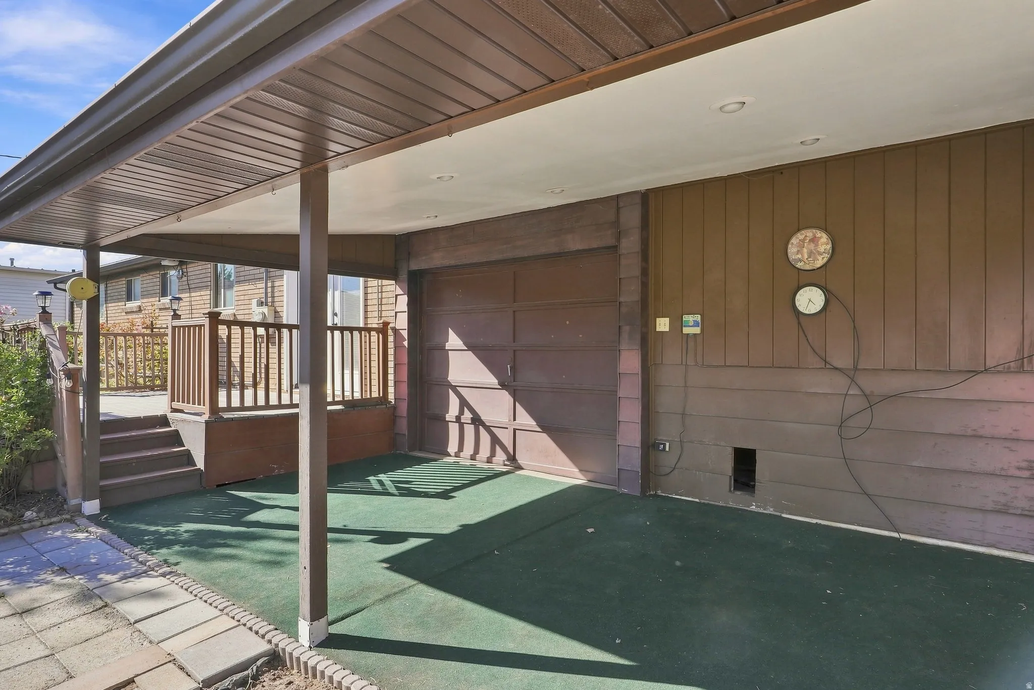 Covered carport with recessed lighting, integrated garage door, and direct access to an elevated wooden deck with railings