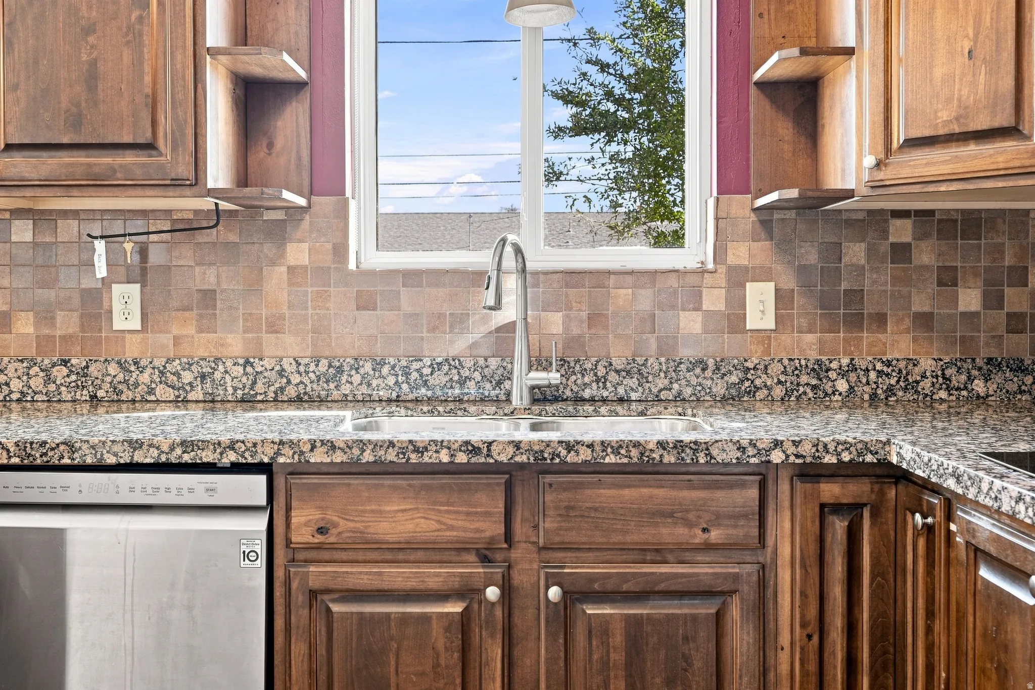 Kitchen featuring wood cabinetry, a stainless steel dishwasher, a double basin sink with a gooseneck faucet, a mosaic tile backsplash, and granite countertops