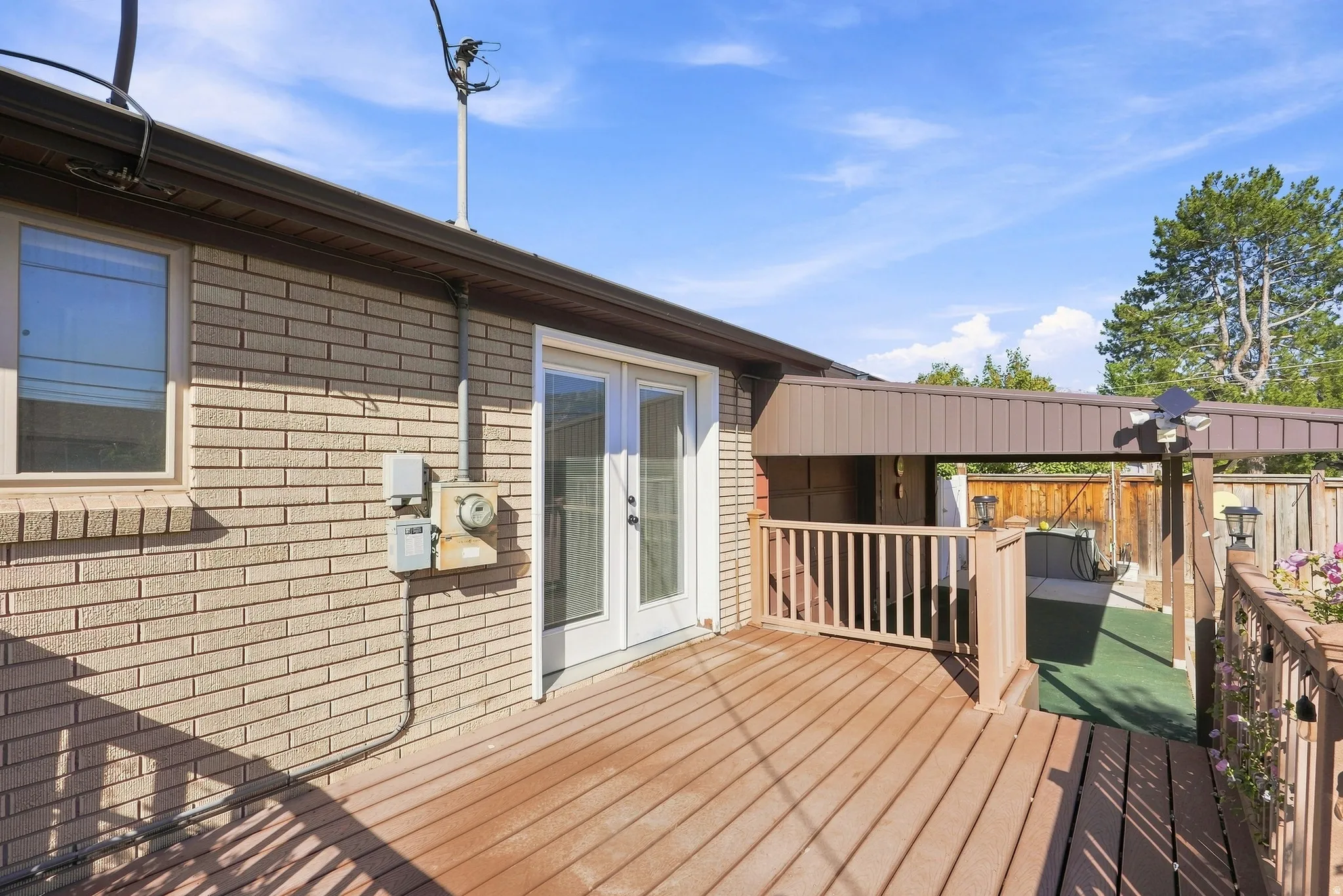 Expansive wood-finish deck with white double French doors, a covered patio area, and a wood privacy fence