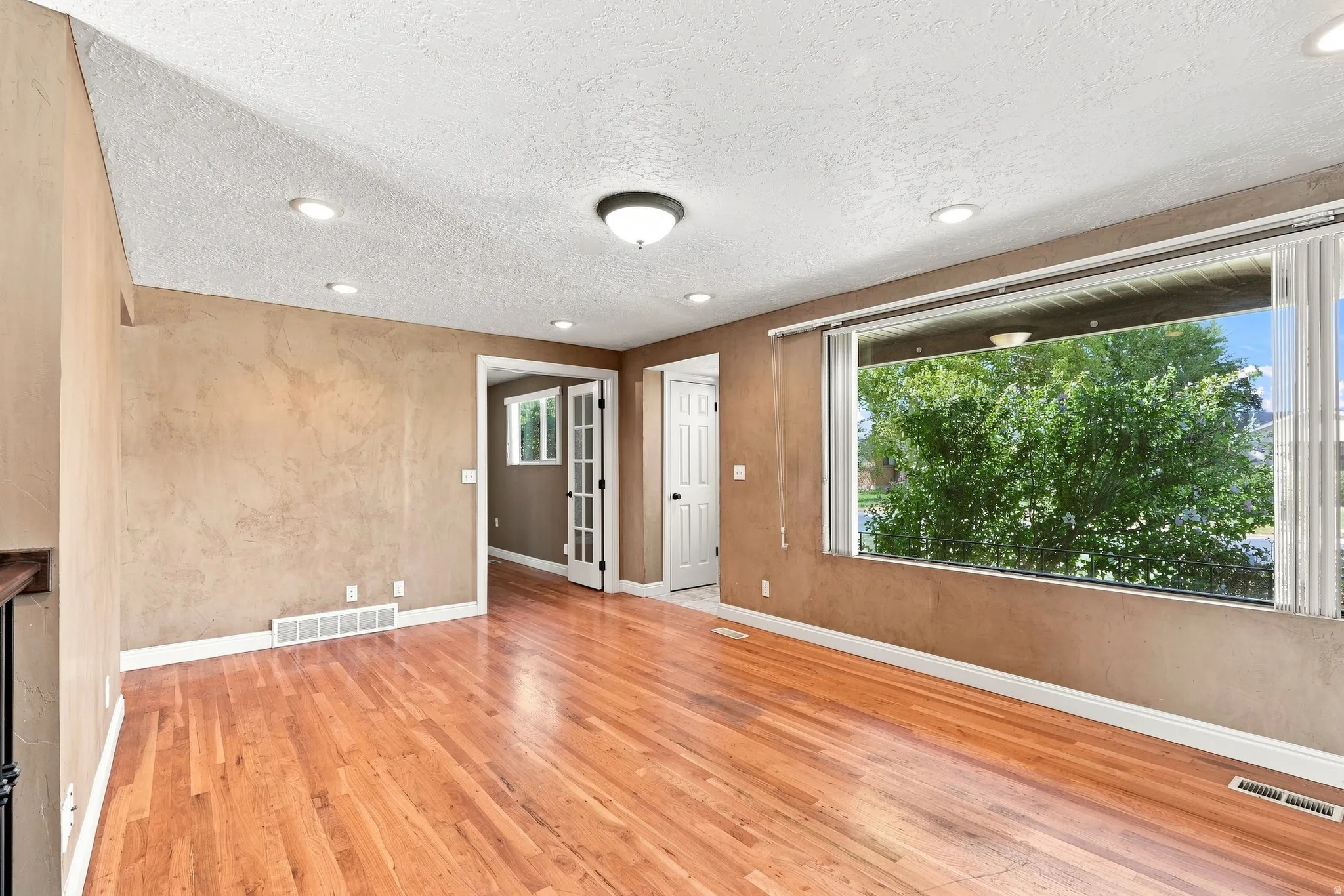 Hardwood flooring, recessed lighting, large window with blinds, ceiling-mounted light fixture, and white trim throughout