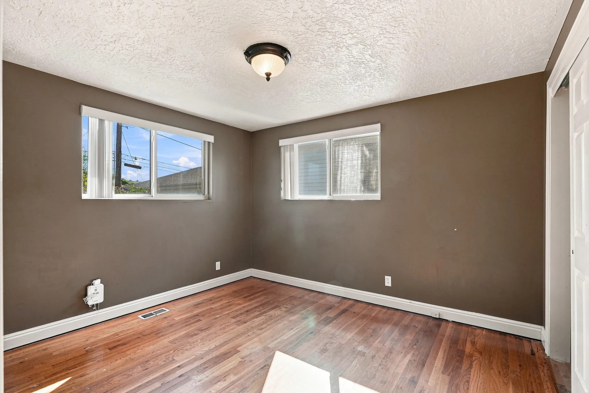 Wood-finish flooring, two windows with white frames, white baseboards, and a semi-flush mount ceiling light fixture
