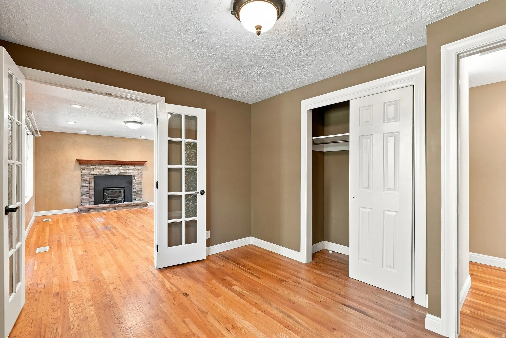 Wood-finish flooring throughout, French doors, recessed lighting, and a stone-clad fireplace with wood mantle