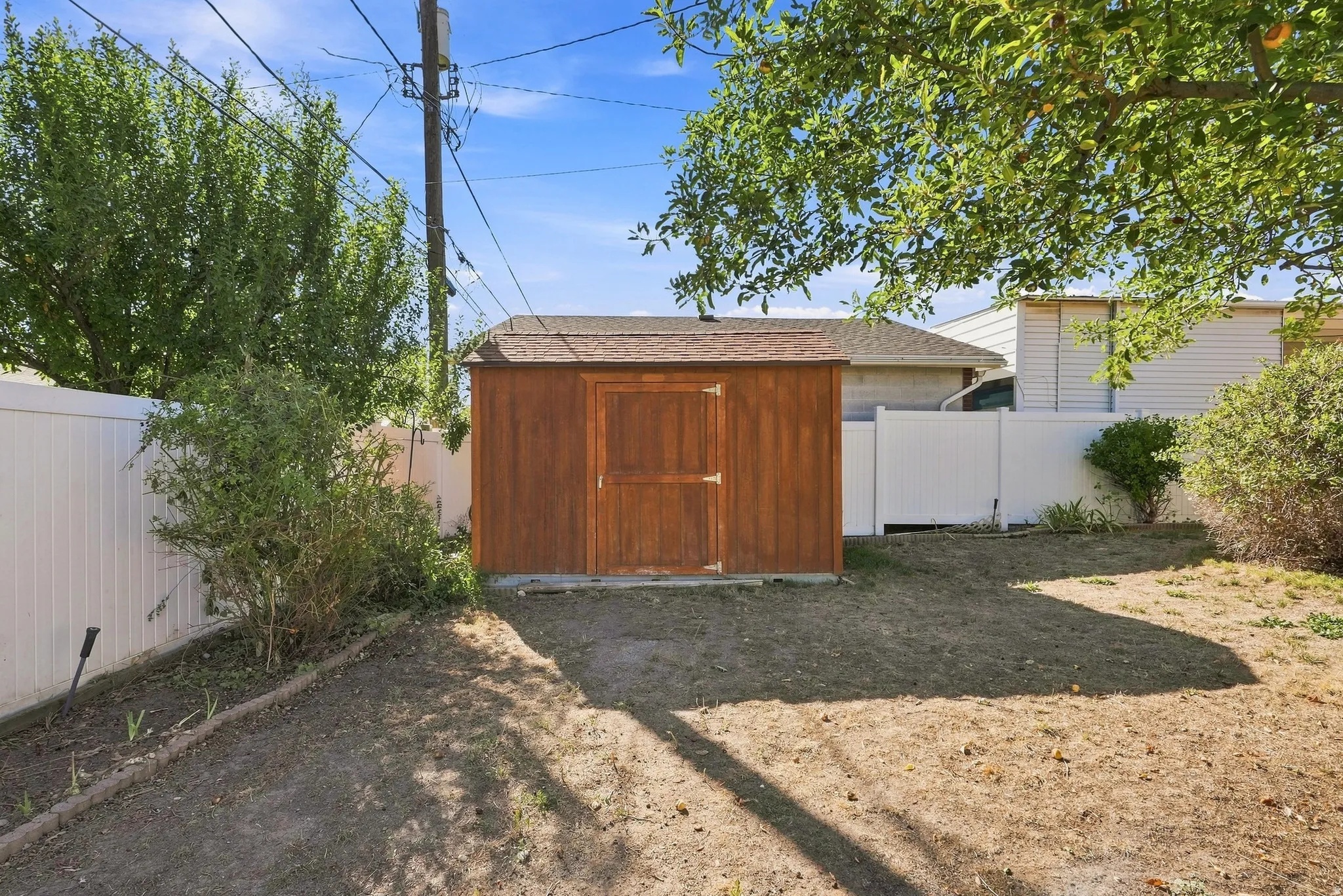 Private backyard featuring a wood storage shed, white privacy fencing, and established trees