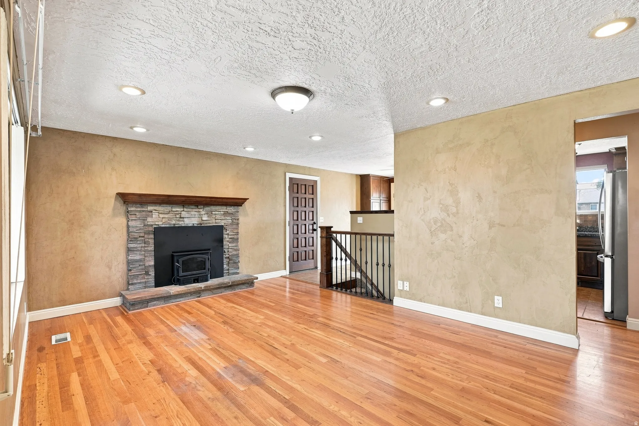 Hardwood flooring, stone-clad fireplace with wood mantle, recessed lighting, and a wood-paneled door