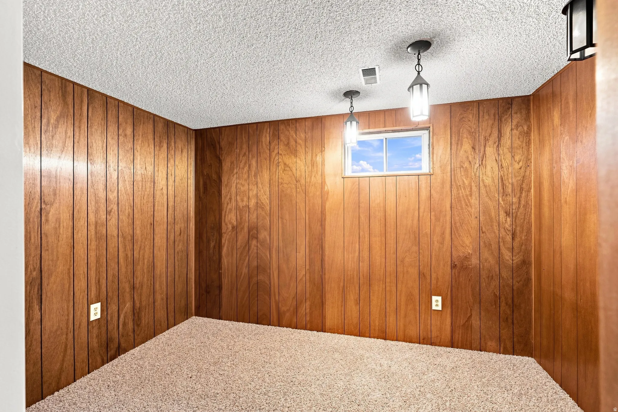 Wood paneling, textured ceiling, carpet flooring, recessed window, and pendant lighting fixtures