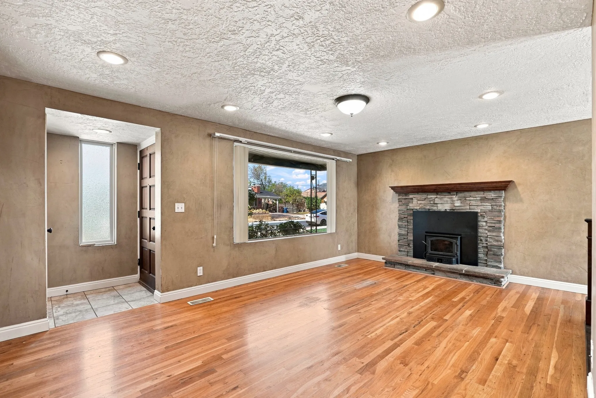 Wood-finish flooring throughout, stone-clad fireplace with wood mantle, recessed lighting, and a front entry with tile flooring and a multi-pane door