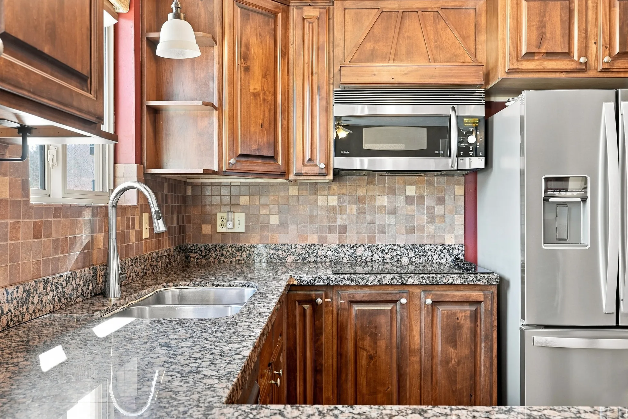 Integrated stainless steel microwave, double basin sink with gooseneck faucet, full-height tile backsplash, wood-finish cabinetry, and stone countertops