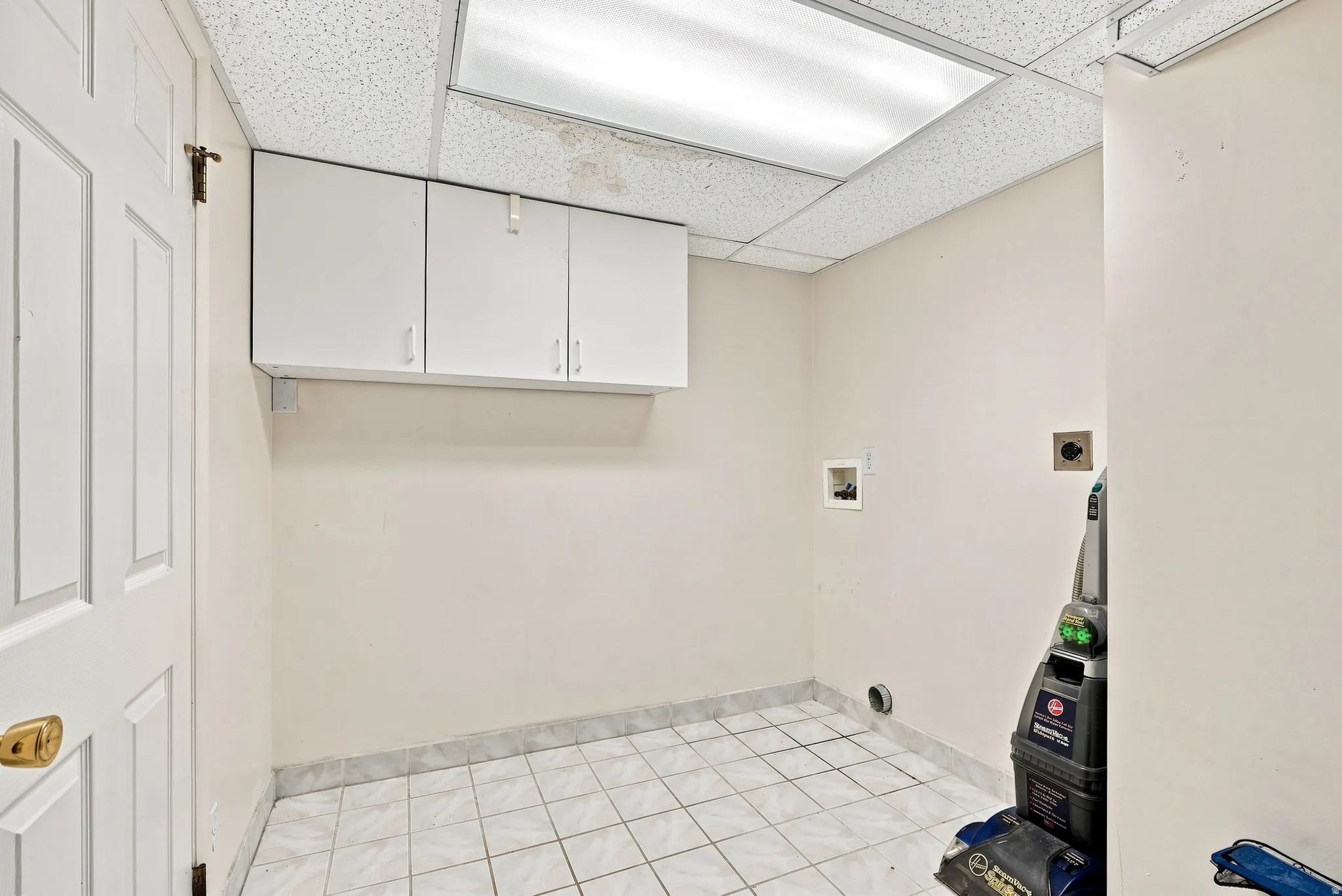White paneled door with brass hardware, upper white cabinetry, tiled flooring, and drop ceiling with recessed lighting
