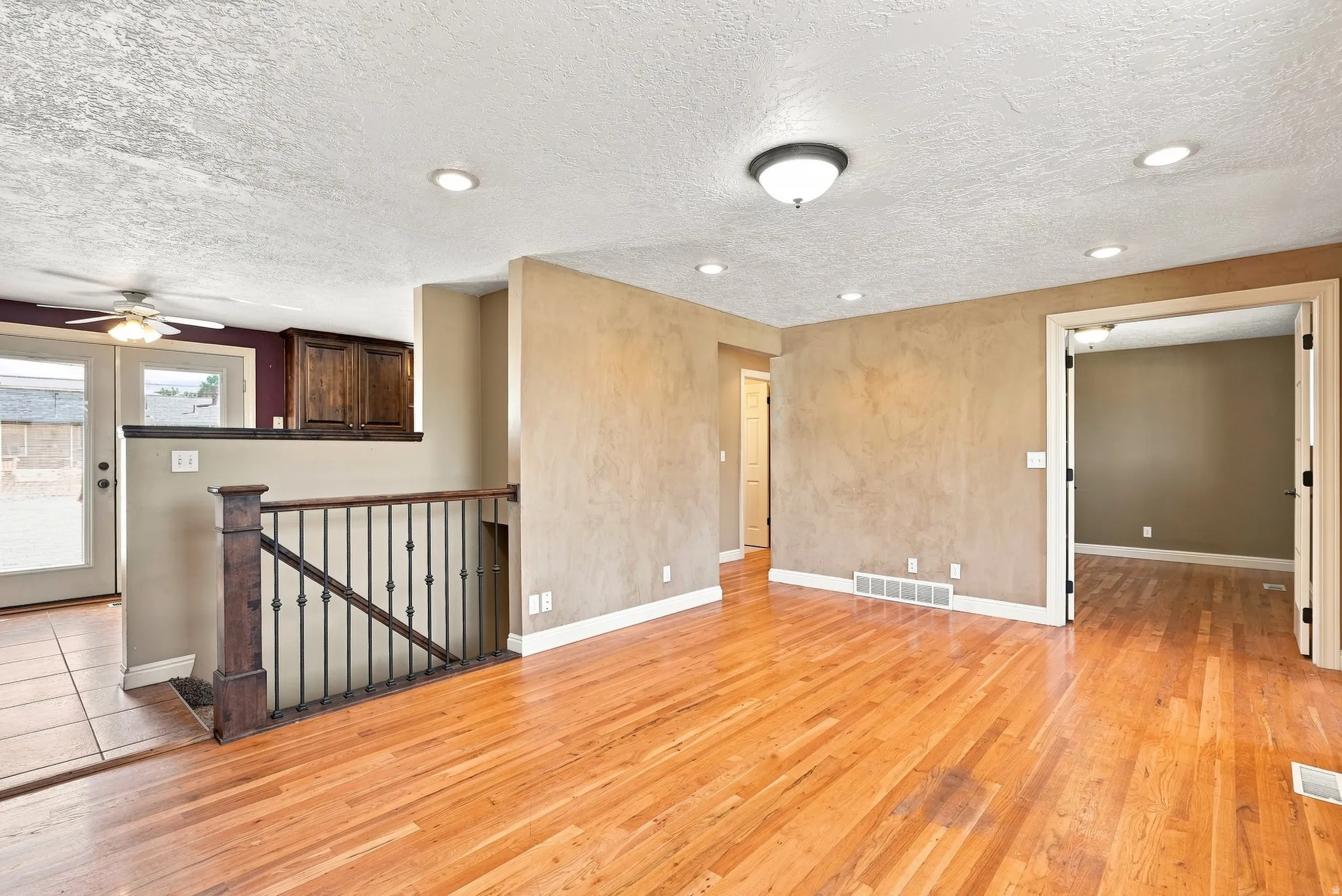 Hardwood flooring throughout, recessed lighting, and a wrought iron railing with wood newel post