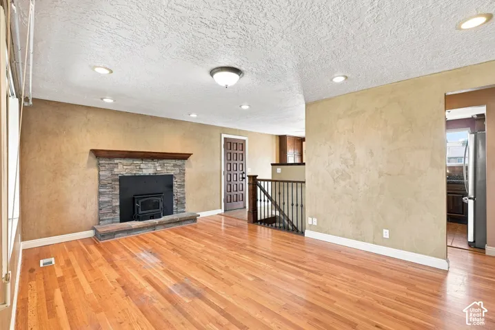 Hardwood flooring, stone-clad fireplace with wood mantle, recessed lighting, and a wood-paneled door