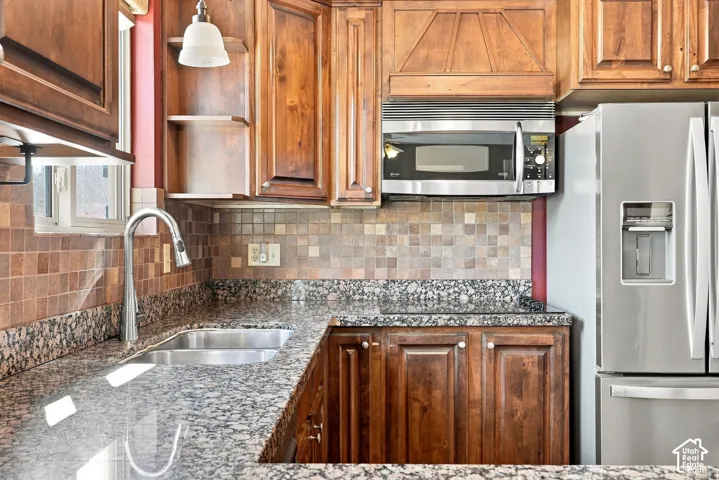 Integrated stainless steel microwave, double basin sink with gooseneck faucet, full-height tile backsplash, wood-finish cabinetry, and stone countertops