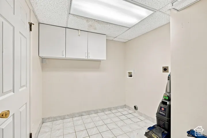 White paneled door with brass hardware, upper white cabinetry, tiled flooring, and drop ceiling with recessed lighting