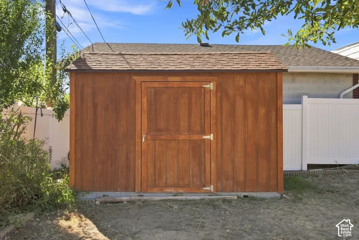 Wooden shed featuring a single door entry, shingle roof, and a gravel perimeter