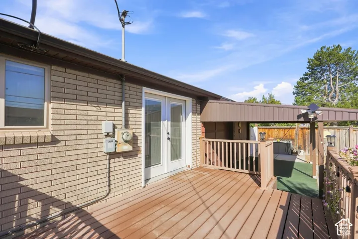 Expansive wood-finish deck with white double French doors, a covered patio area, and a wood privacy fence