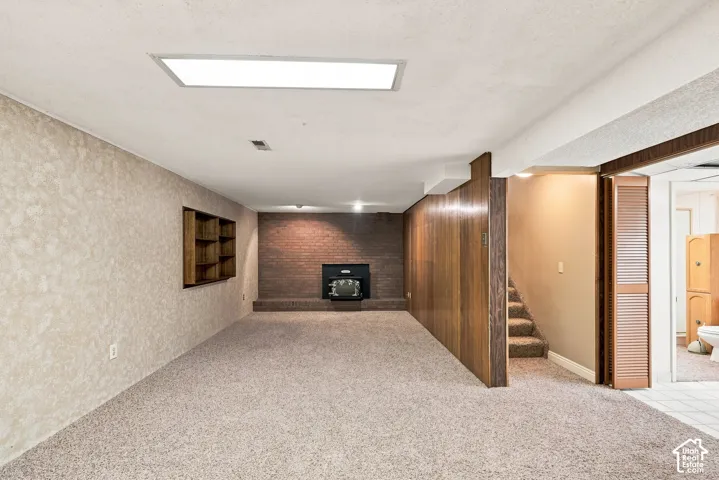 Carpeted floor, wood paneling, recessed lighting, built-in shelving, and a brick fireplace