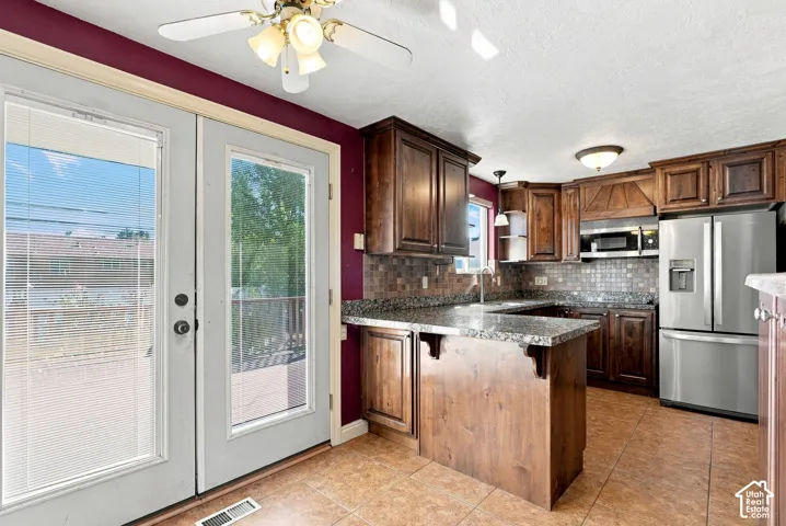 Kitchen featuring wood cabinetry, stainless steel appliances, a granite-finish countertop, a tile backsplash, and a center island