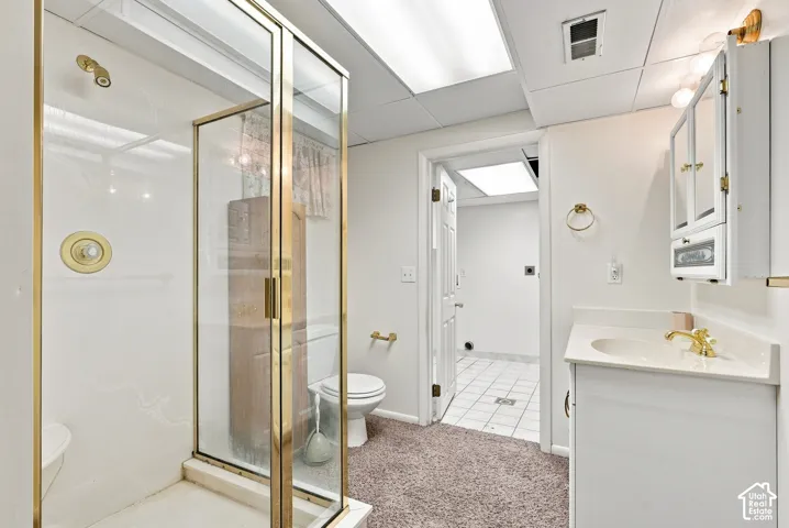 Enclosed shower with brass-finish framing, vanity with integrated sink, wall-mounted medicine cabinet, recessed lighting, and tile flooring