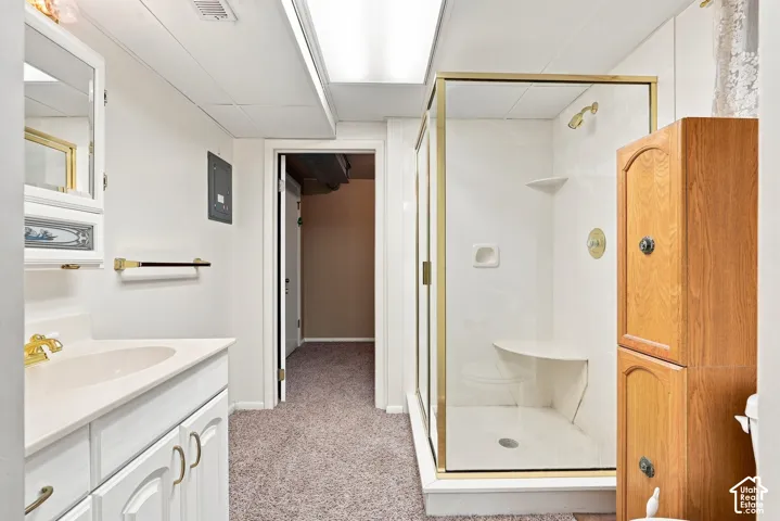 Bathroom featuring a white vanity with integrated sink, gold-tone fixtures, a glass-enclosed shower with gold-tone frame, and a wood-finish storage cabinet